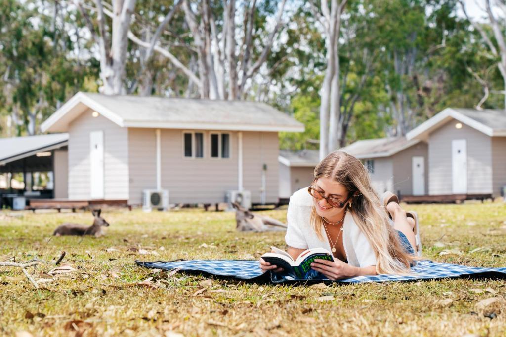 Cootharaba的住宿－KangaROOMS Noosa Everglades YHA，躺在草地上读书的女人