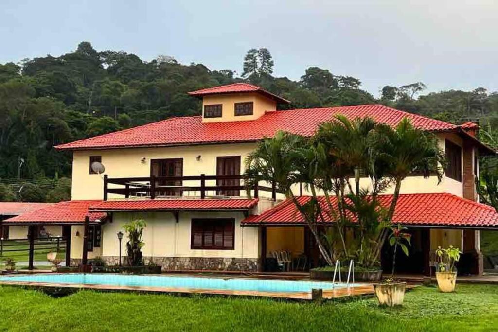 帕蒂杜阿爾費里斯的住宿－Sítio com 3 suítes +3 quartos, campo e piscina.，一座红色屋顶的房子和一个游泳池