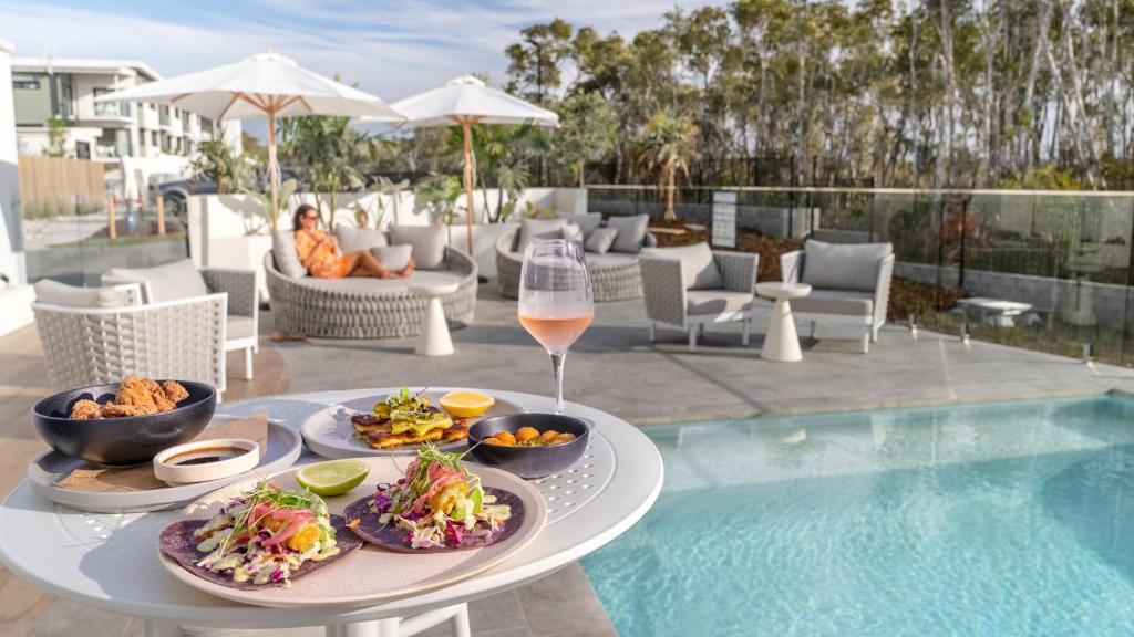 einen Tisch mit Essen und ein Glas Wein neben einem Pool in der Unterkunft Essence Peregian Beach Resort - Wallum 4 Bedroom Luxury Home in Peregian Beach
