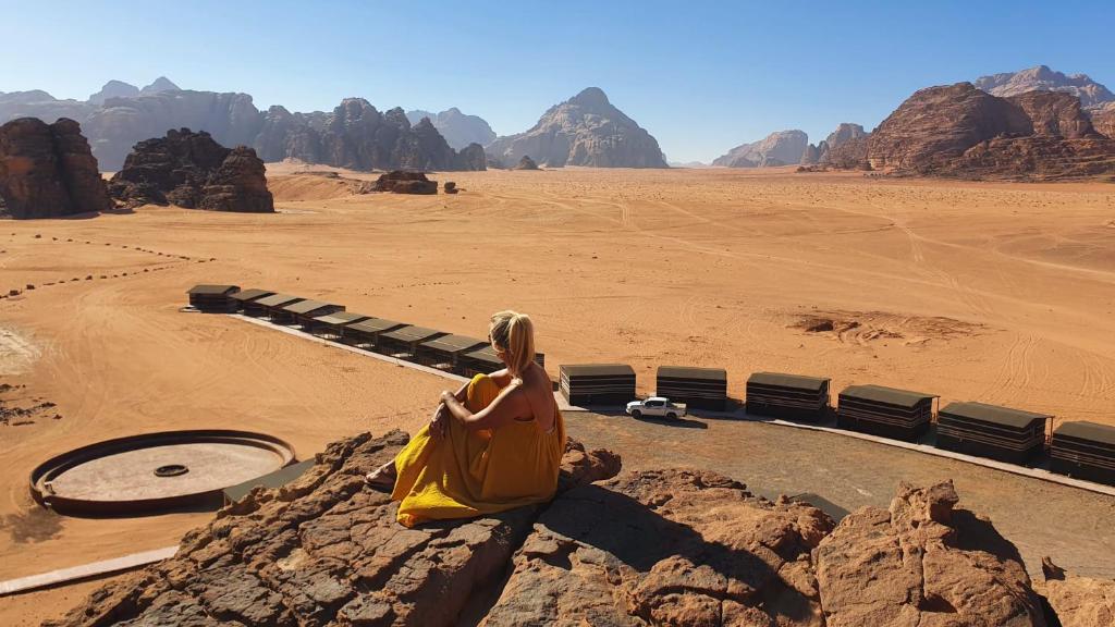 een vrouw zittend op een rots in de woestijn bij Rum Under The Stars Camp in Wadi Rum