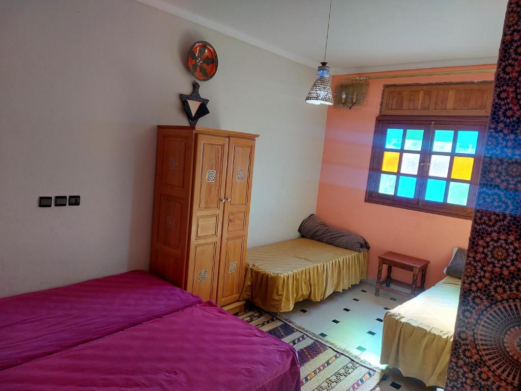 1 dormitorio con 2 camas, armario y ventana en Gite Rahhaoui Simo, en Kasba des Aït Moussa