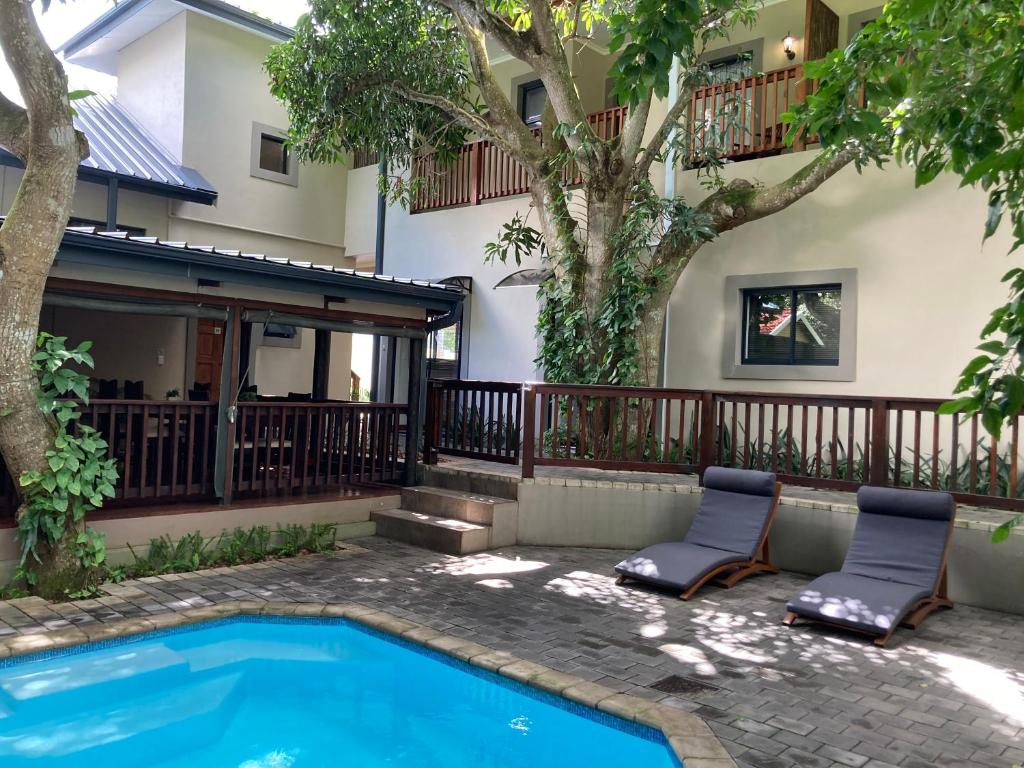 St Lucia的住宿－Turaco Guest House，一座建筑物前的游泳池,旁边设有两把椅子