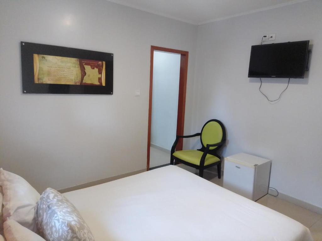 a bedroom with a bed and a chair and a television at Hospedaria U in Lobito