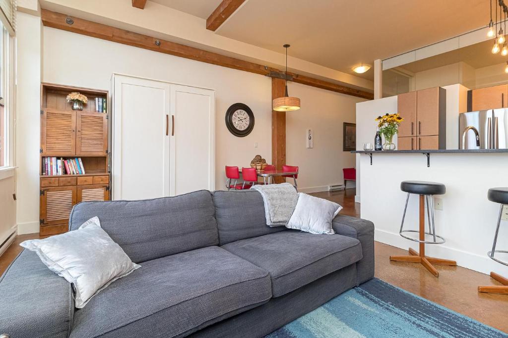 a living room with a gray couch and a kitchen at Modern Heritage Studio With Murphy Bed in Victoria
