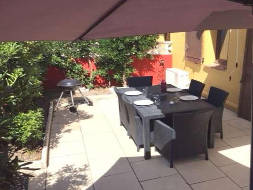 un patio con mesa, sillas y sombrilla en Maison Caraïbes en Le Barcarès