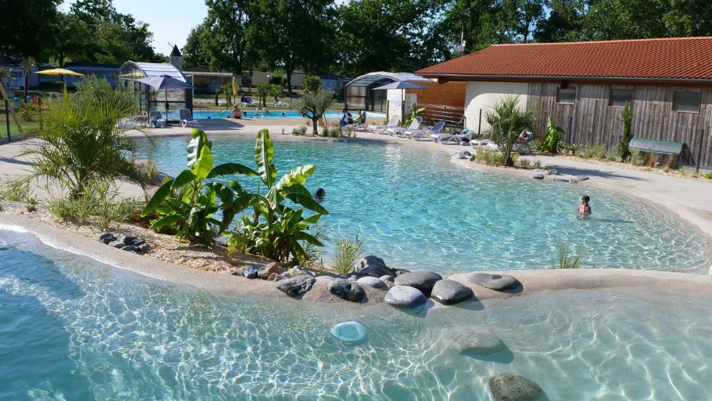 a pool with rocks and a person in the water at Mobil Home XXL 4 chambres - Camping du Vieux Moulin in Vensac