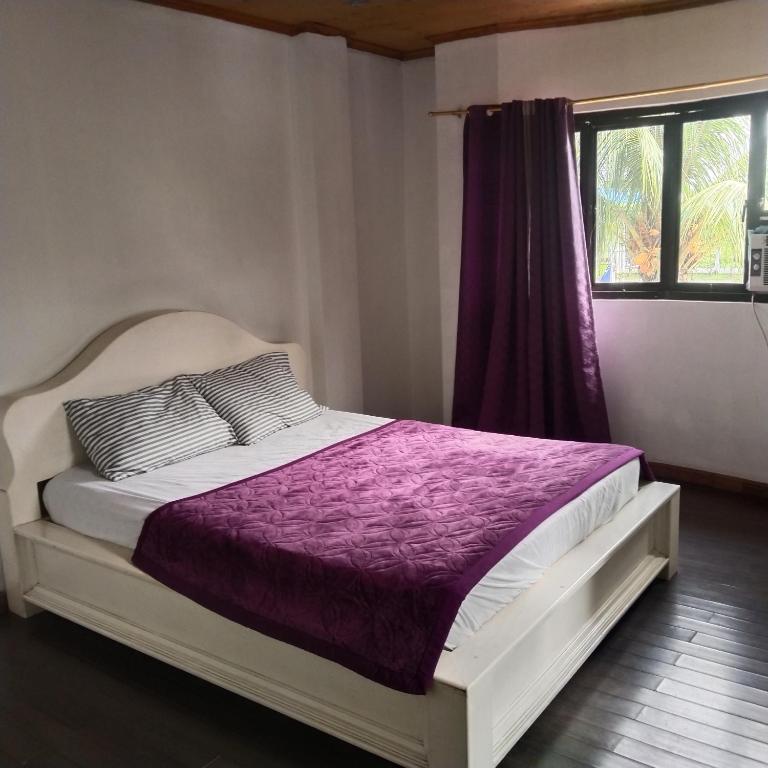 una camera da letto con un letto con lenzuola viola e una finestra di Madria's Pension House Reddoorz a Tumauini