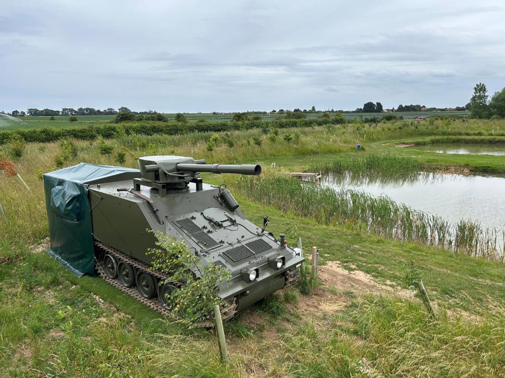 a tank parked in a field next to a body of water at The Tank in Friskney