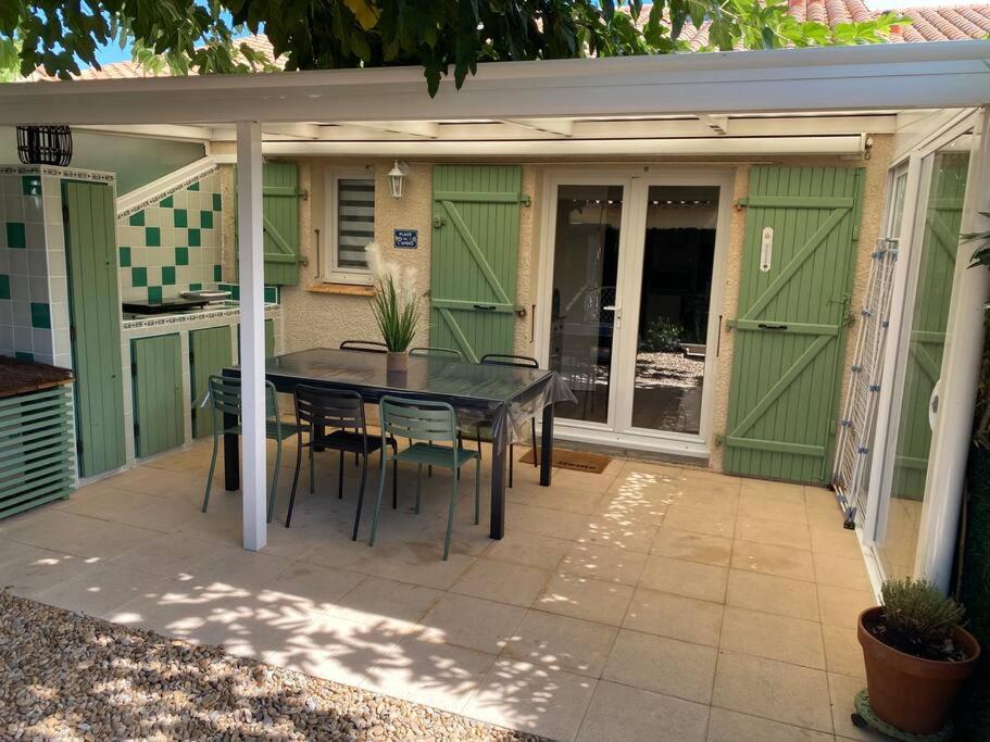 d'une terrasse avec une table, des chaises et des portes vertes. dans l'établissement Maison de plage - 6 pers - clim - parking, à Frontignan