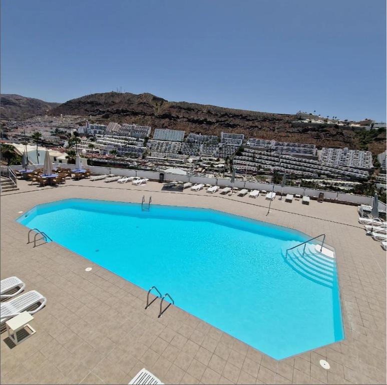 a large blue swimming pool with lounge chairs and buildings at Arimar Sun 13 Puerto Rico in Puerto Rico de Gran Canaria