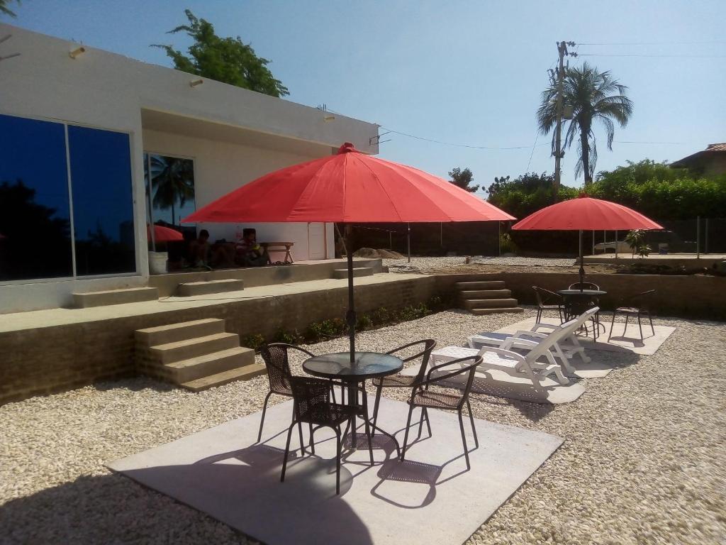 two tables and chairs with red umbrellas in front of a building at Hostal Mi Elvirula in Santa Marta