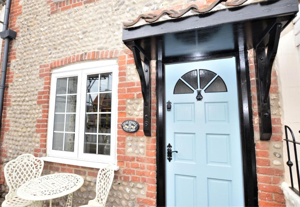 a brick house with a blue door and a table and chairs at Cockleshell Cottage in Sheringham