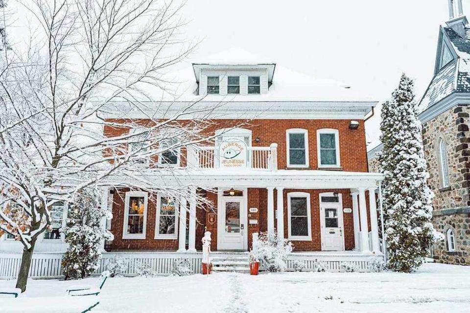a red brick house with a snow covered yard at Auberge de Jeunesse Magog-Orford Hostel in Magog-Orford