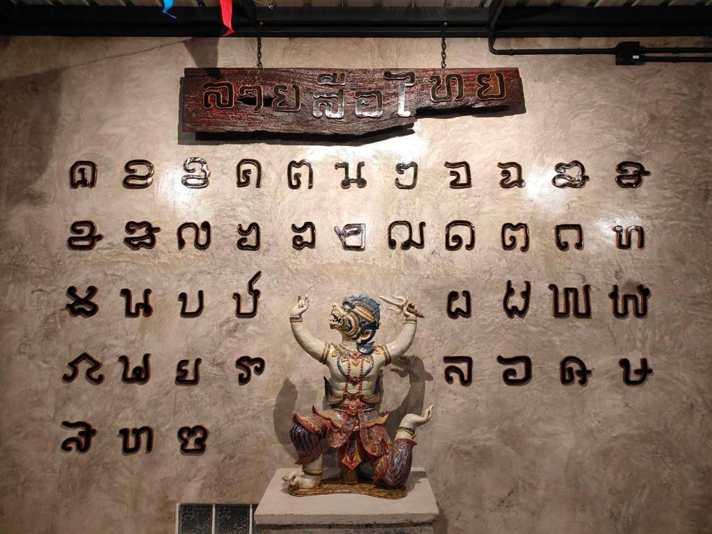 uma escultura de uma mulher com um alfabeto na parede em Smilingface guesthouse em Sukhothai