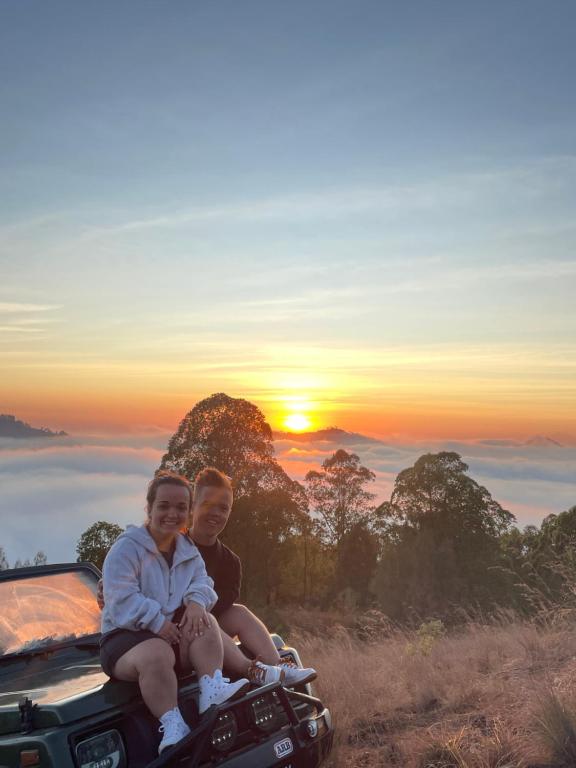 a man and a woman sitting on the hood of a truck with the sunset at Batur volcano sunrise jeep in Kubupenlokan