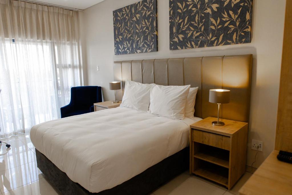 a bedroom with a large white bed and a chair at Acres Inn Klerksdorp in Klerksdorp
