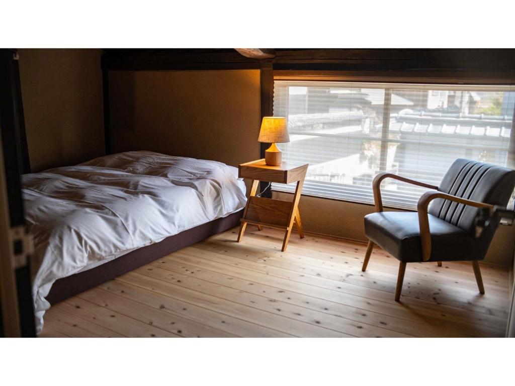 a bedroom with a bed and a chair and a window at Kominka Hotel kurasu - Vacation STAY 24260v in Tatsuno