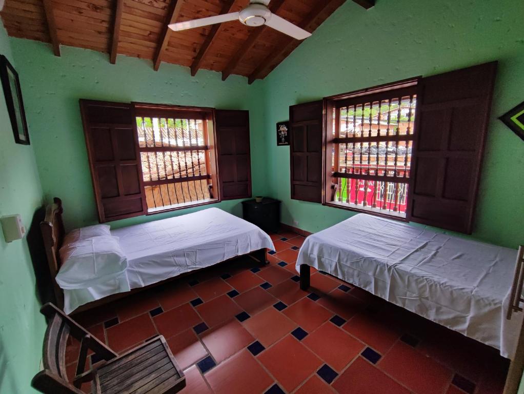two beds in a room with green walls and windows at Hostal La Pola in Santa Fe de Antioquia