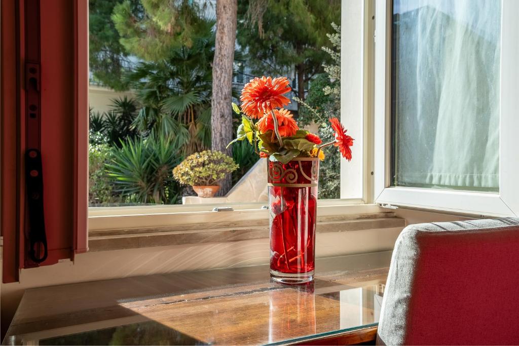 eine rote Vase mit Blumen auf einem Tisch im Fenster in der Unterkunft B&B Cumpari Turiddu in Syrakus