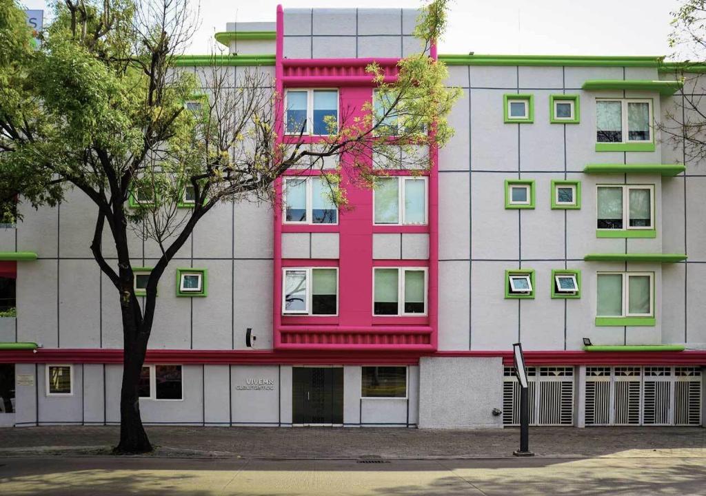 un edificio rosa y blanco con un árbol delante en Estancias VIVE MX en Ciudad de México