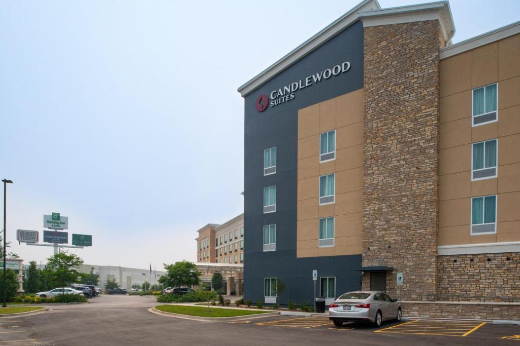 a building with a car parked in a parking lot at Candlewood Suites - Joliet Southwest by IHG in Joliet