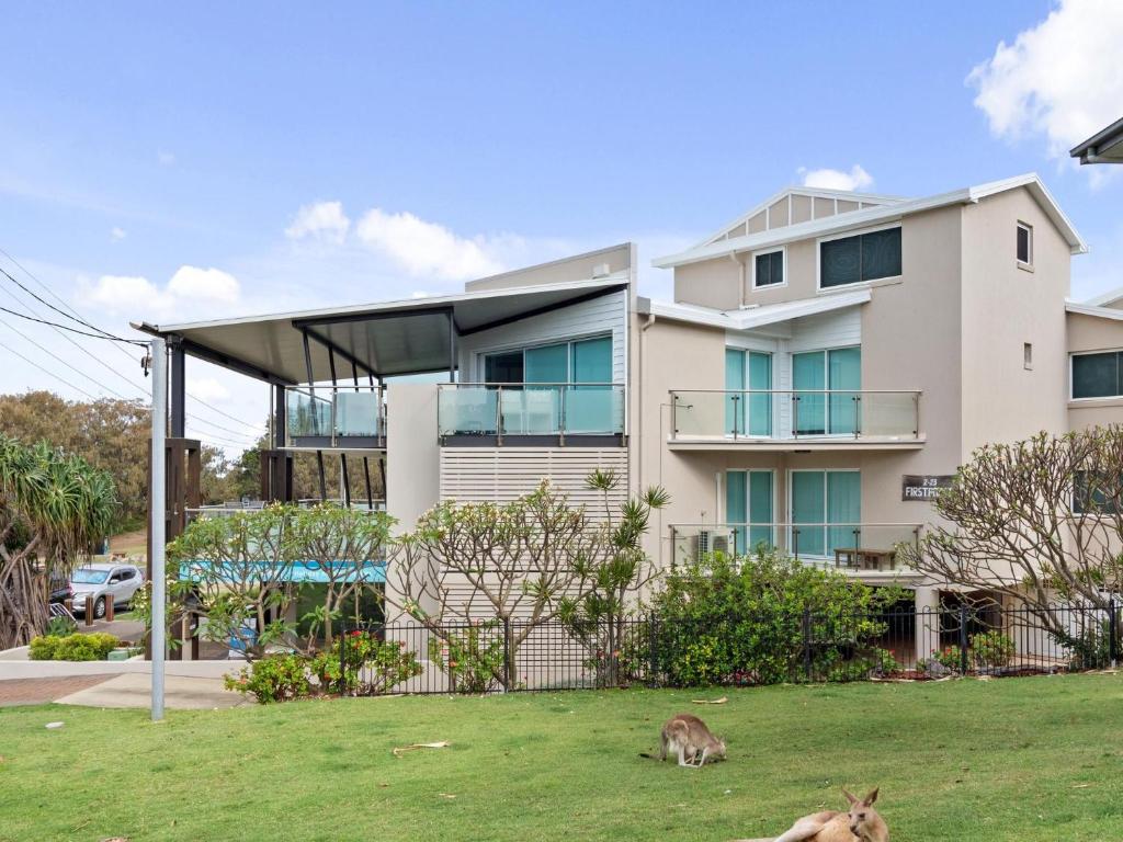a cat laying in the grass in front of a house at First Point Down by Discover Stradbroke in Point Lookout