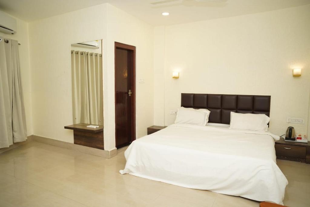 1 dormitorio con 1 cama blanca grande y espejo en VIRAMMA RESORT en Siliguri