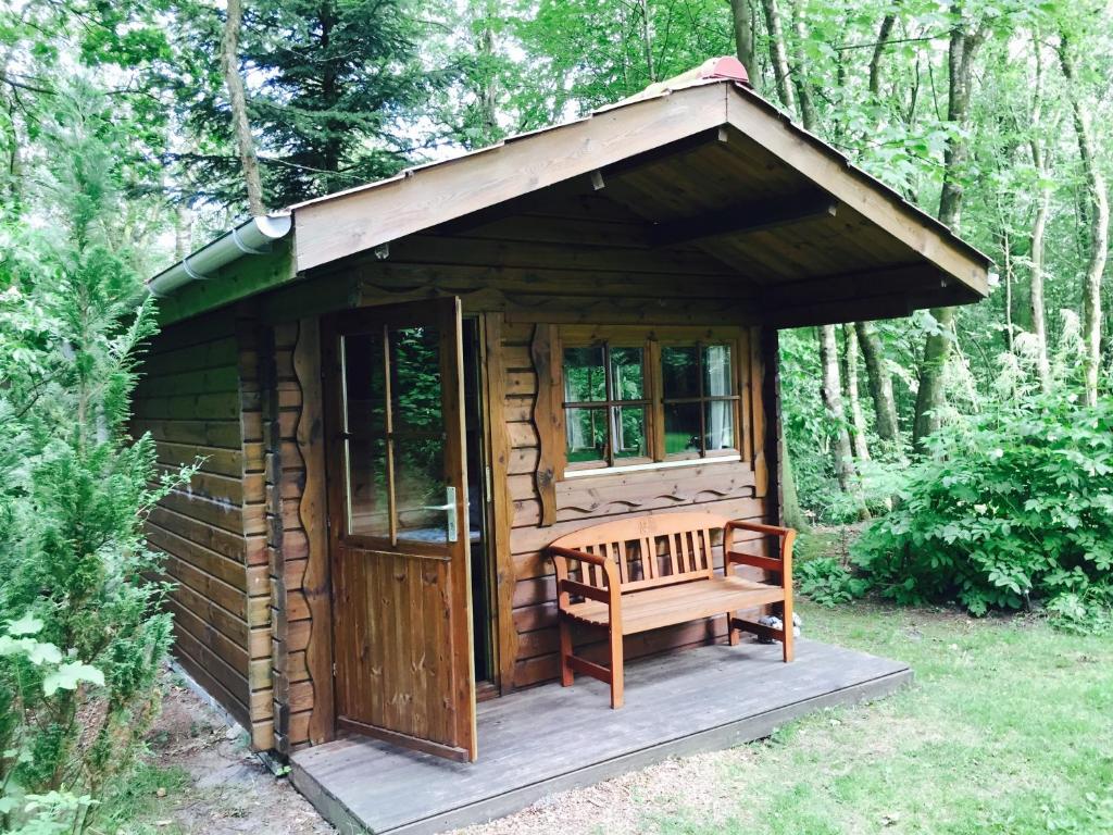 une cabane en bois avec un banc dans les bois dans l'établissement Krogager Primitiv Camping - Krogen, à Grindsted