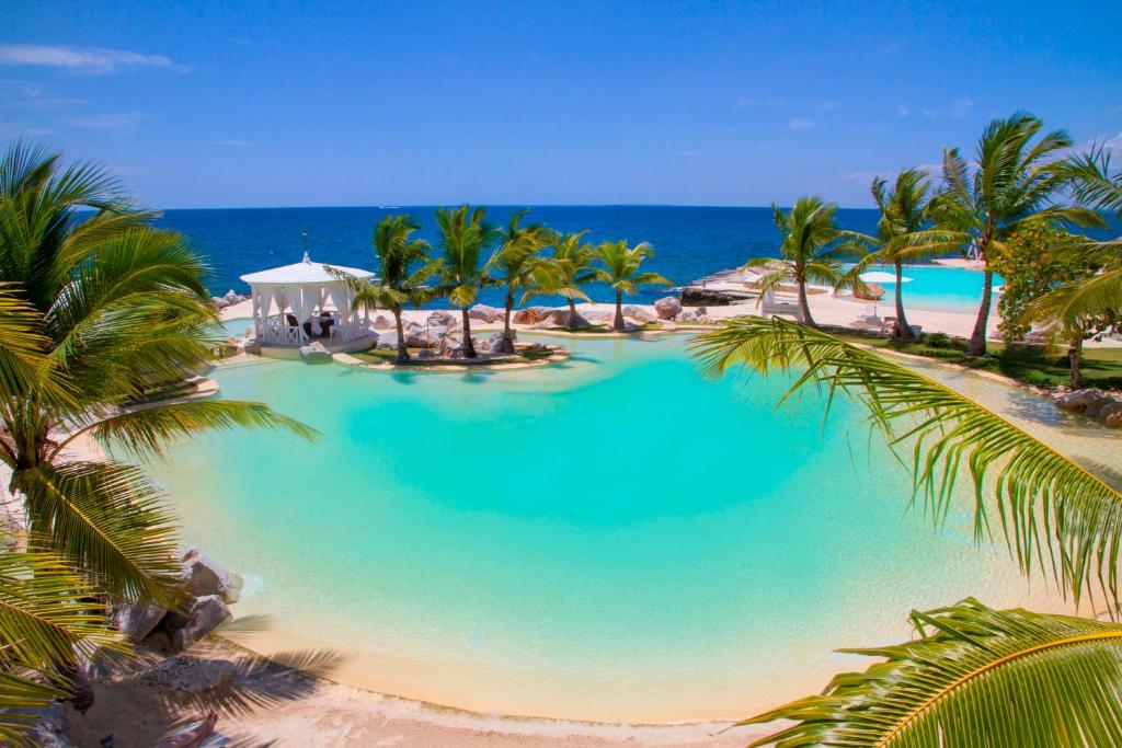 une grande piscine avec des palmiers et l'océan dans l'établissement Tracadero Beach Resort, à Bayahibe