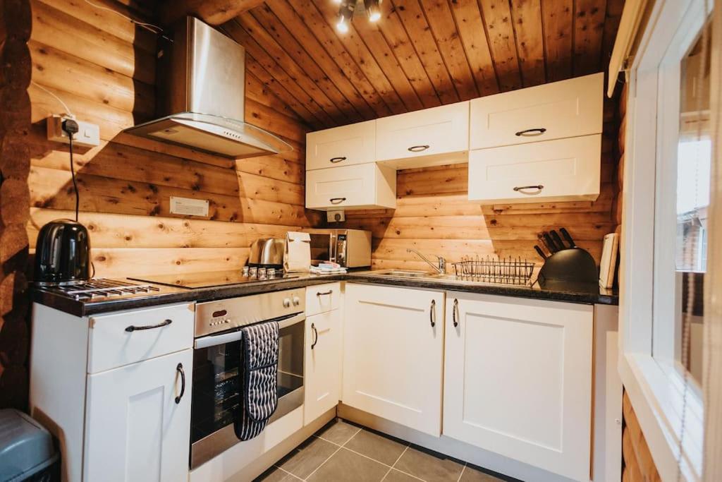 a kitchen with white cabinets and wooden walls at Rural Log Cabin in Snowdonia - 2 Bedrooms & Parking in Ffestiniog