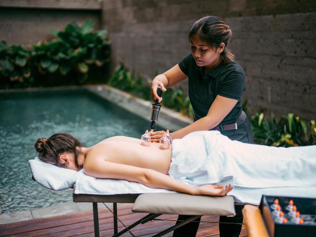 a woman giving a man a massage in front of a pool at Secana Beachtown Resort & Residences in Canggu