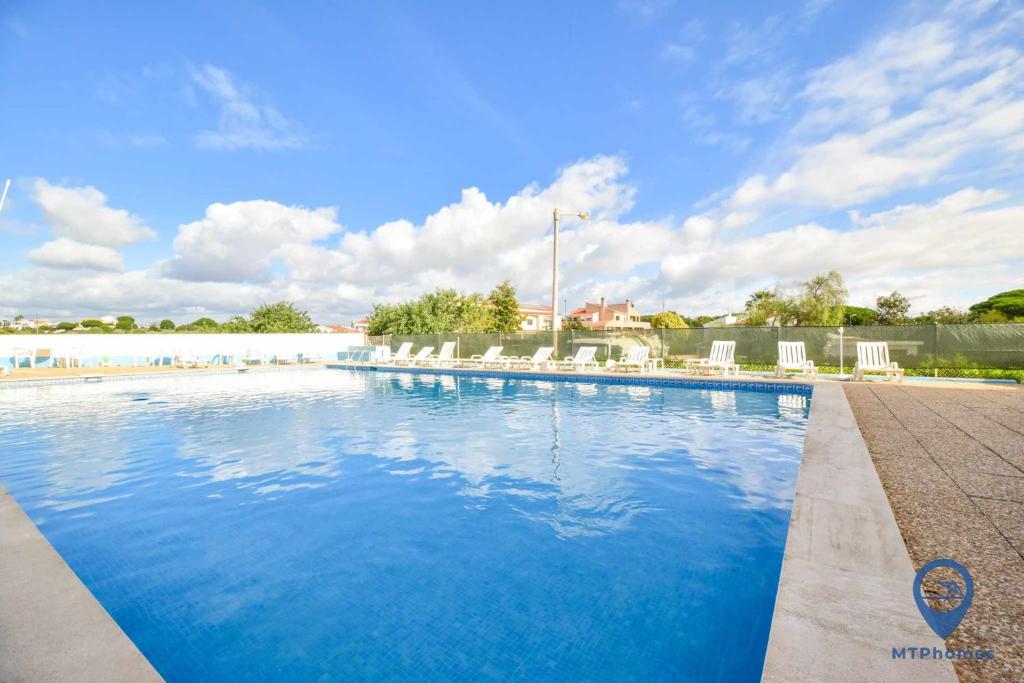 a large swimming pool with white chairs and blue water at Apartamento 2 quartos e Piscina in Olhos de Água