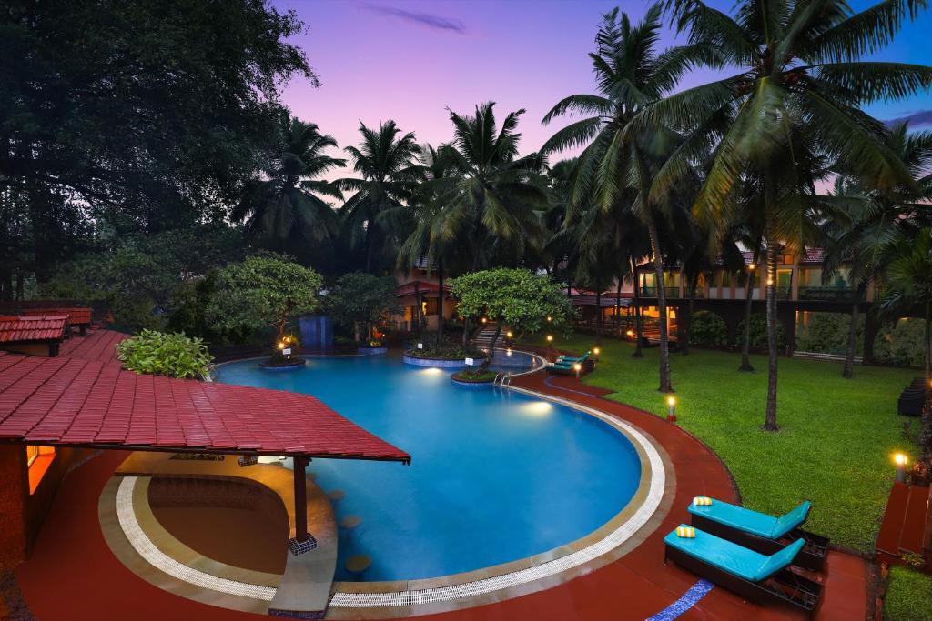 a resort pool with chairs and palm trees at night at Lemon Tree Amarante Beach Resort, Goa in Candolim