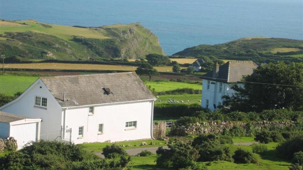 une maison blanche dans un champ avec l'océan dans l'établissement Middleton Hall Cottage, à Rhossili