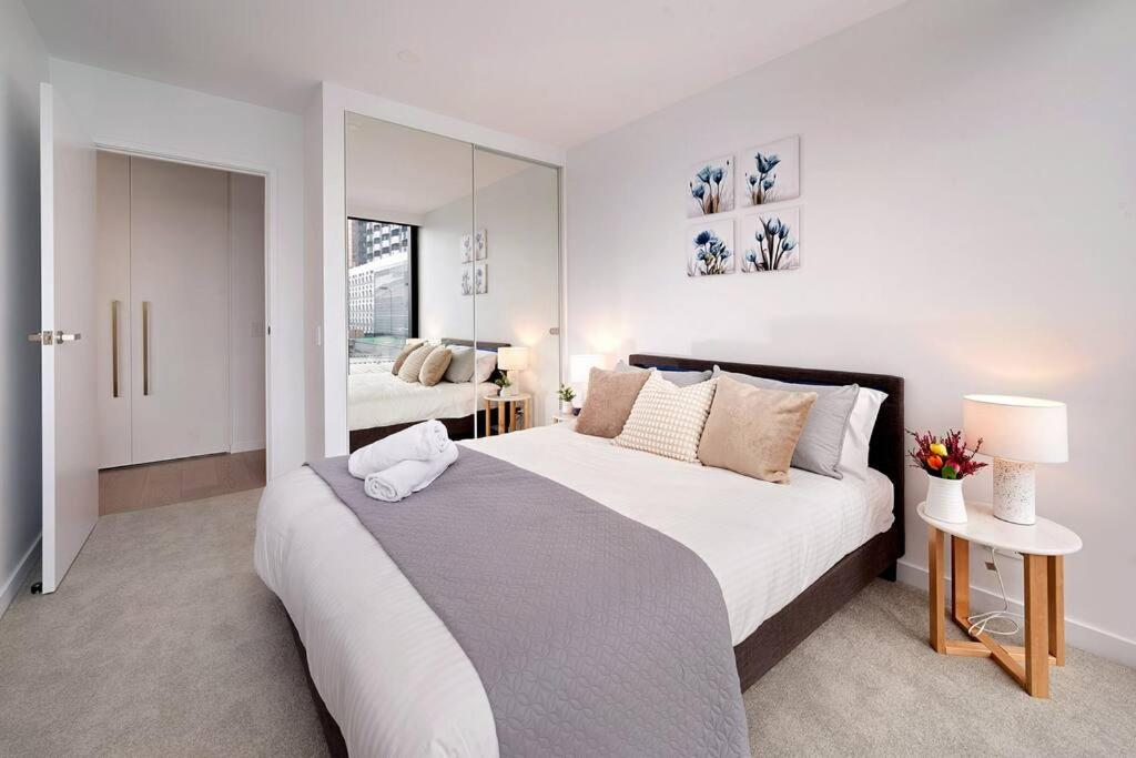 a white bedroom with a large bed and a mirror at Chic 1BR1B w BBQ, GYM, walk to Box Hill Central in Box Hill