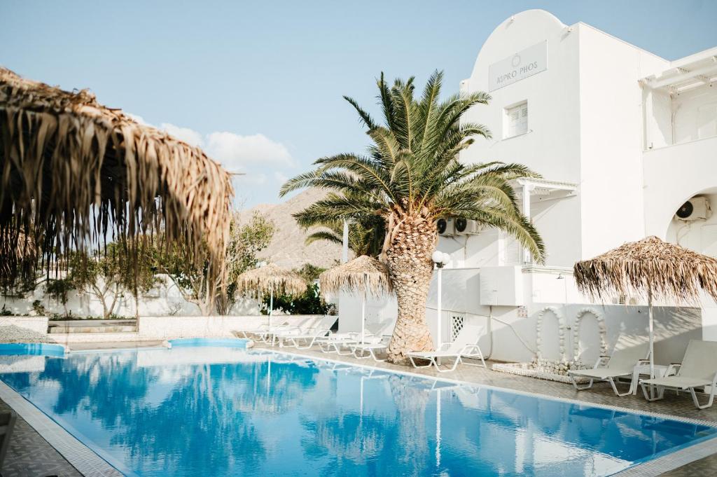 a pool at a hotel with palm trees and chairs at Aspro Phos Santorini Hotel in Perissa