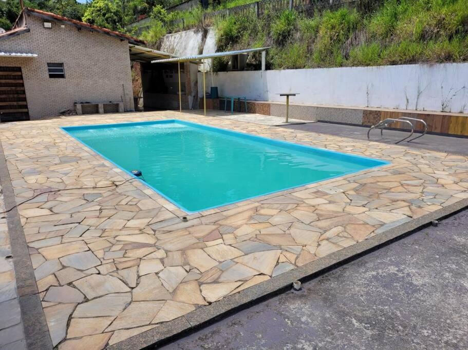 uma piscina com piso de pedra e água azul em Sítio Elo Perdido Guararema em Guararema