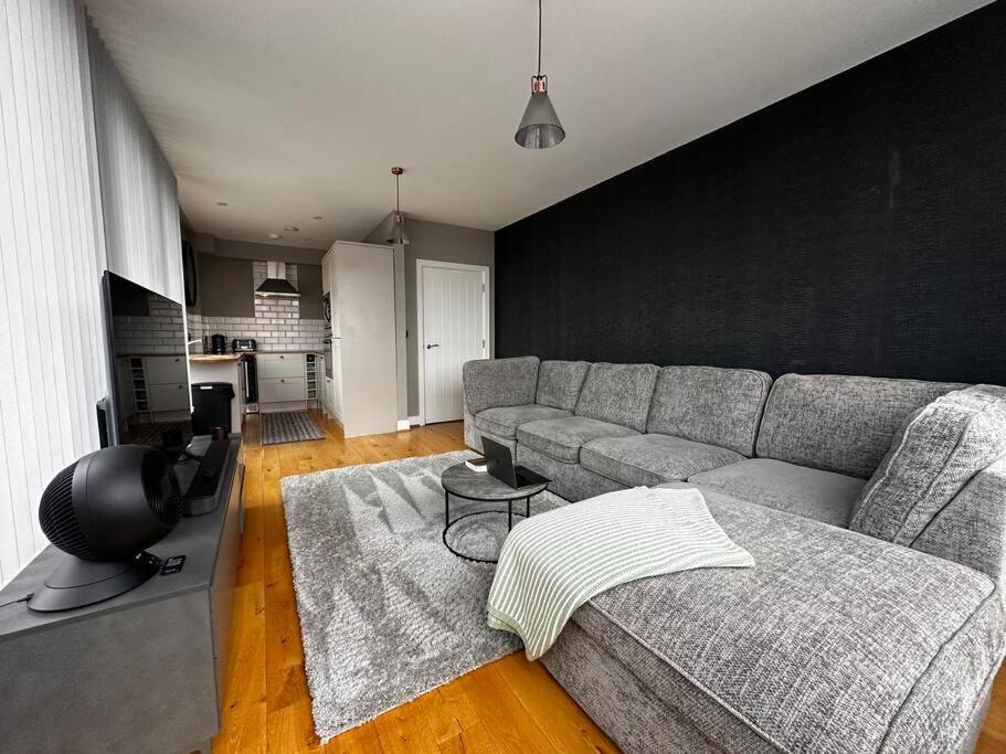 a living room with a gray couch and a kitchen at Luxury Penthouse Apartment in Uxbridge