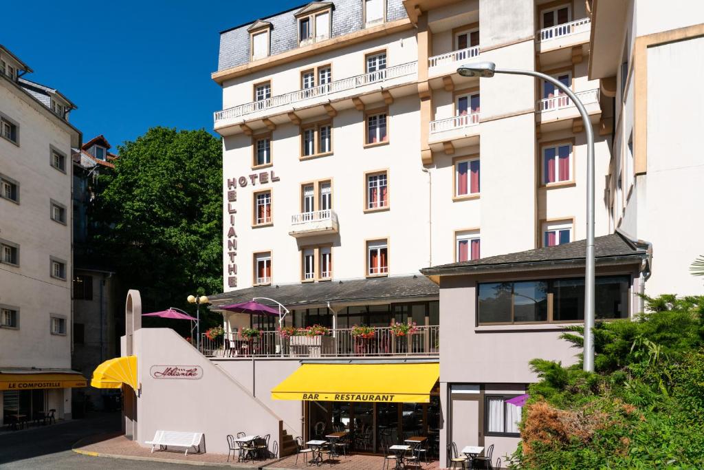ルルドにあるHôtel Héliantheの白い大きな建物で、目の前にレストランがあります。