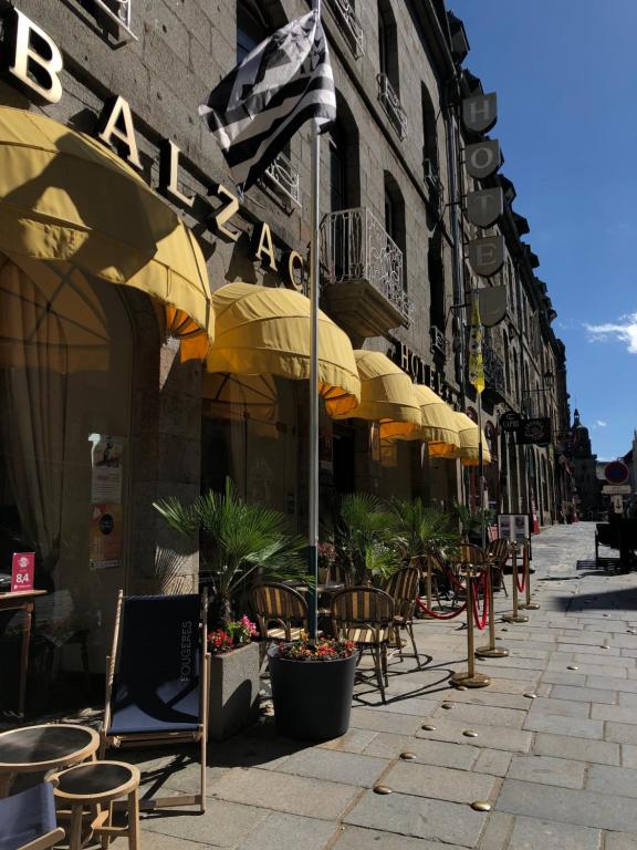 una calle con mesas, sillas y sombrillas en Balzac Hôtel en Fougères