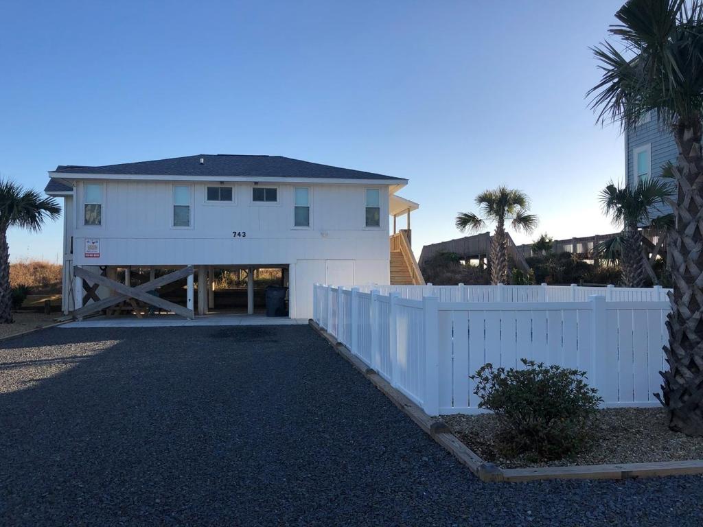 uma casa branca com uma cerca e palmeiras em Meant To Be home em Holden Beach