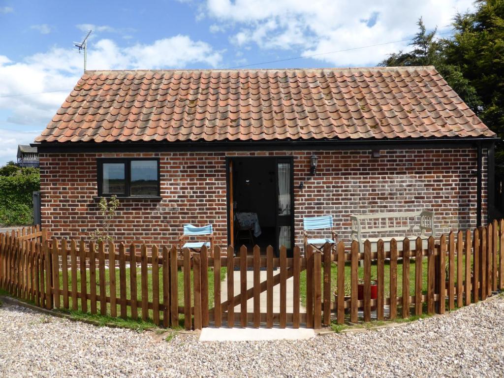 una pequeña casa de ladrillo con una valla de madera en Hay Barn en Winterton-on-Sea