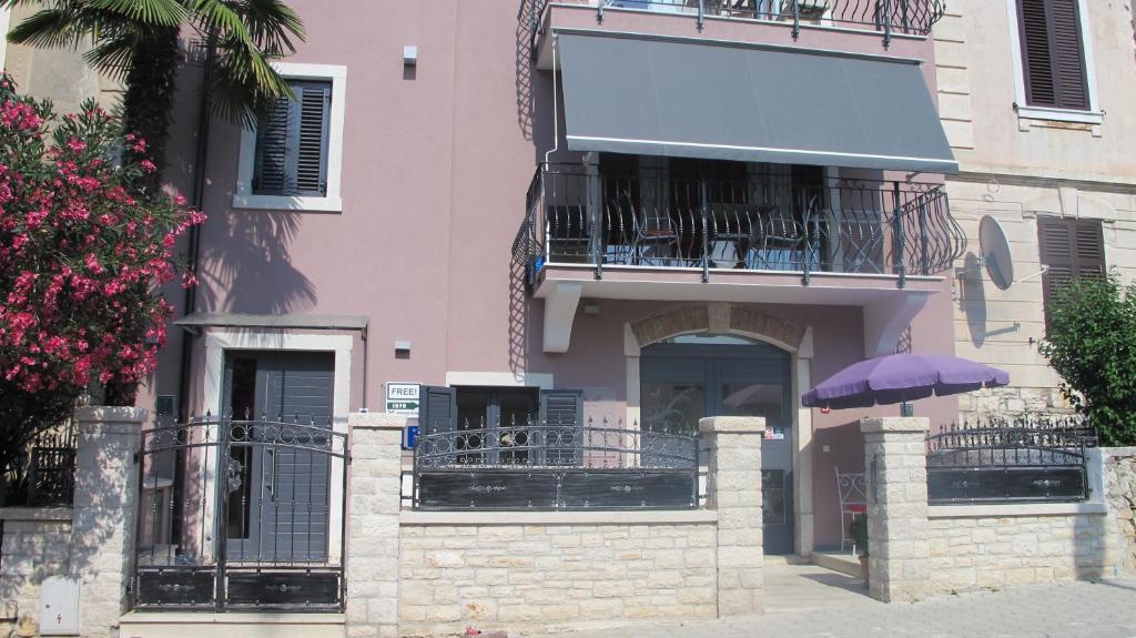 a pink building with a balcony and a purple umbrella at Kseni Accommodation in Rovinj