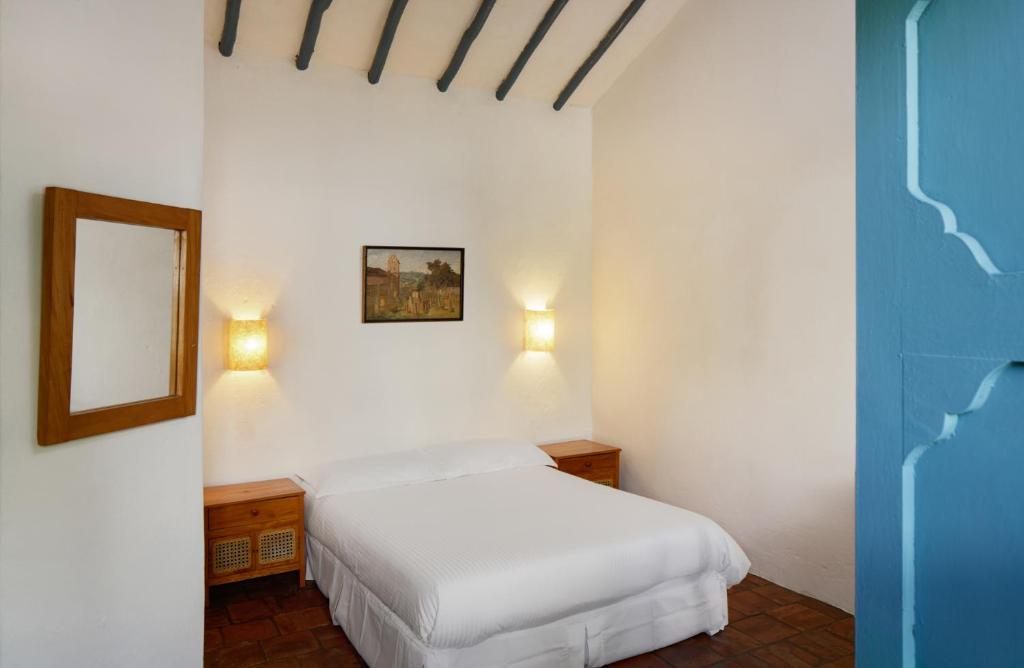 a white bedroom with a bed and a mirror at Posada del Campanario in Barichara
