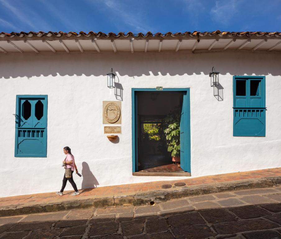 a woman walking past a building with blue doors at Posada del Campanario in Barichara