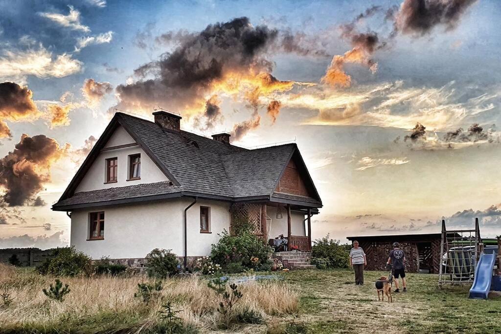 een huis in een veld met twee mensen en twee honden bij W Korcu Maku - dom wakacyjny in Rutka Tartak