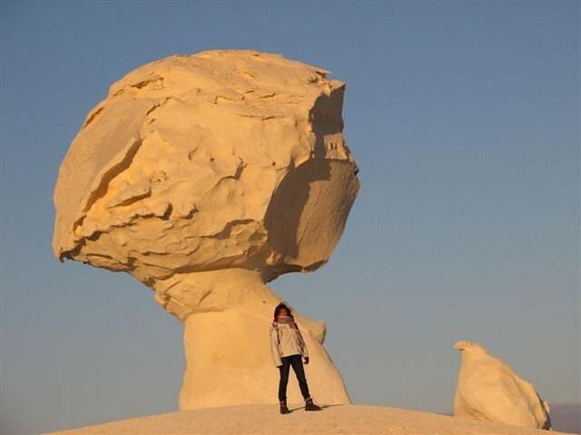 a person standing in front of a large rock at White desert & Black desert camb in Qasr Al Farafirah