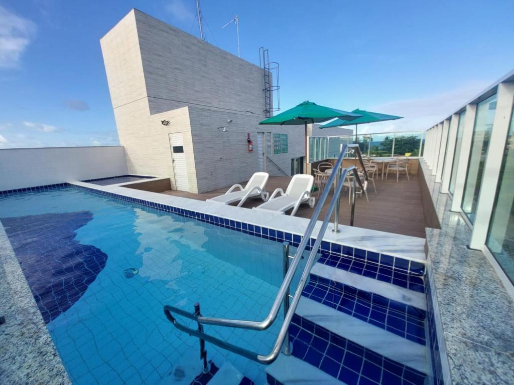 a swimming pool with chairs and an umbrella at MAKARANDUBA BEACH 304 - Piscinas Naturais e Coração de Porto in Porto De Galinhas