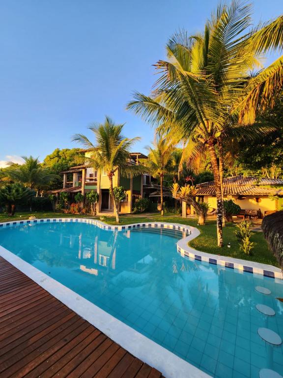 a swimming pool with palm trees and a house at Pousada Mayon in Cumuruxatiba