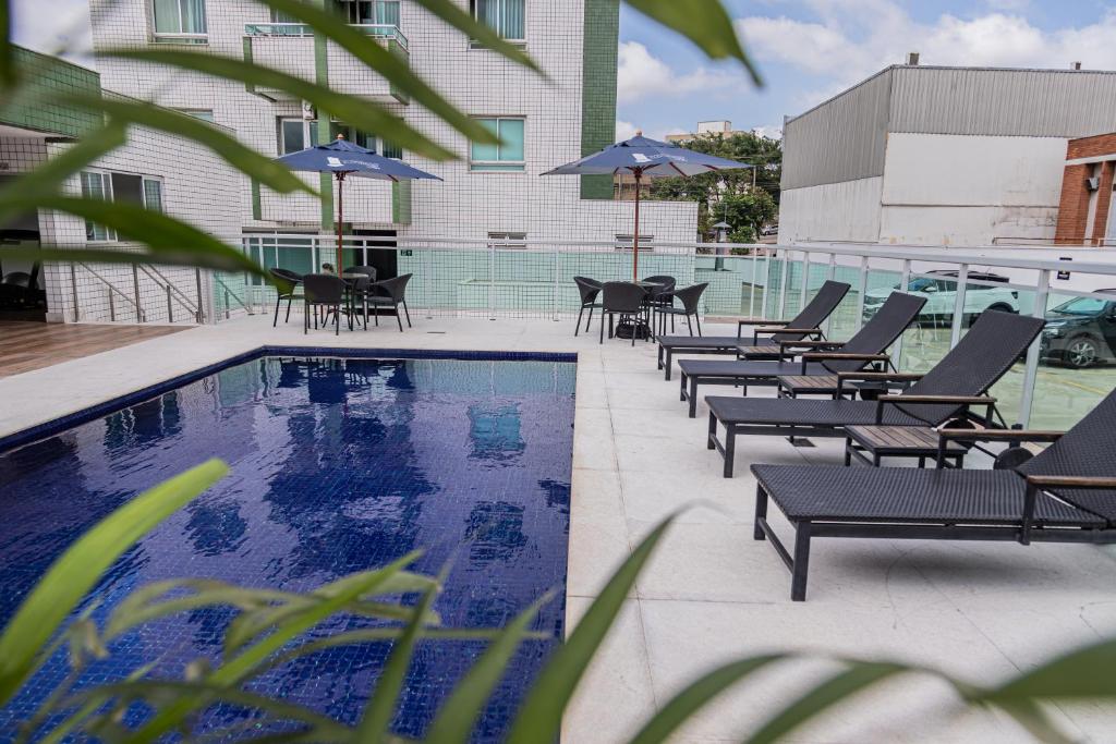 a pool with chairs and umbrellas next to a building at Eldorado Flat in Contagem